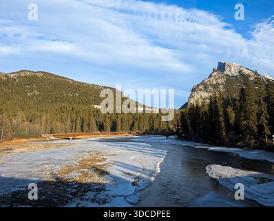 Downtown Banff Avenue The Bow River frozen in winter, with the Rocky Mountains in the background. A popular tourist destination on a sunny winter day. Stock Photo