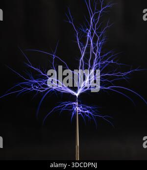 Streams of violet plasma discharge from the top of a Tesla coil in a high-voltage experiment. Stock Photo