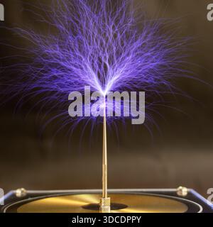 Streams of violet plasma discharge from the top of a Tesla coil in a high-voltage experiment. Stock Photo