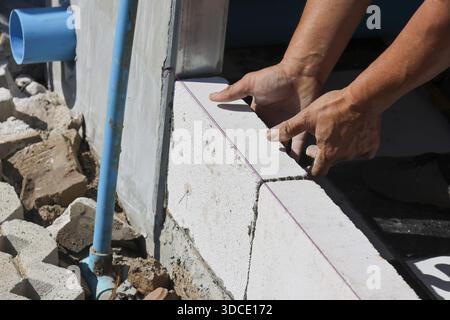 Worker hands installing lightweight white brick block on concrete wall at construction site with focus and precision showing industry craftsmanship co Stock Photo