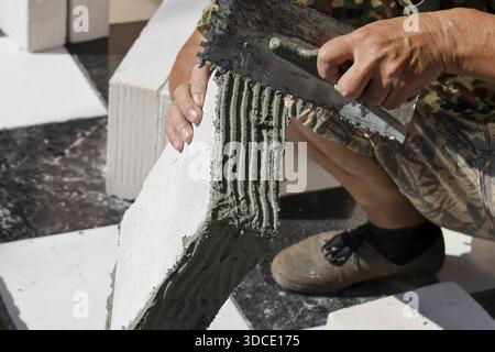 Professional construction worker hand focused installing lightweight white brick masonry with trowel applying cement mortar to build strong concrete w Stock Photo