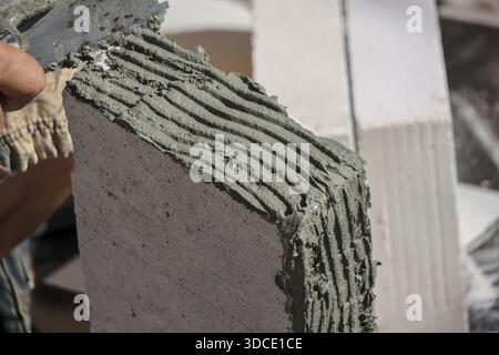 Worker applying thin adhesive mortar on aerated concrete block with notched trowel during wall construction, showing careful precision and focus on bu Stock Photo