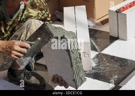 Concentrated construction worker applying adhesive mortar white aerated concrete block with notched trowel for building wall showing careful attention Stock Photo