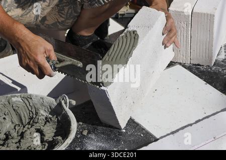Close up view showing construction worker hands diligently applying cement mortar on white lightweight aerated block using notched trowel for building Stock Photo