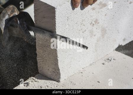 Construction worker focused on cutting autoclaved aerated concrete block with hand saw for building wall at site displaying professional workmanship Stock Photo