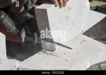 Close up worker hand cutting aerated lightweight concrete block with electric reciprocating saw for building renovation and construction, demonstratin Stock Photo