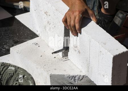 Close up worker hand installing white lightweight concrete block with metal bracket showing focus and dedication on construction site building solid w Stock Photo