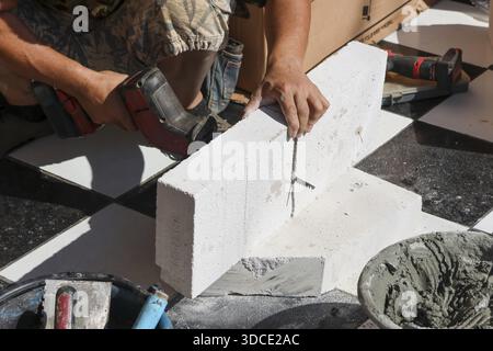 Focused male construction worker cutting white concrete block using electric saw at building site with serious concentration Stock Photo