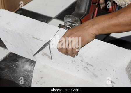 Focused construction worker cutting autoclaved aerated concrete block with electric grinder construction site carefully using angle cutter to shape wh Stock Photo