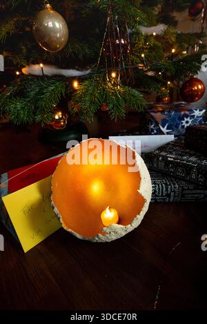 Festive Christmas scene with a glowing candle bowl placed under a decorated tree, surrounded by wrapped gifts and warm lights in a cozy home interior. Stock Photo