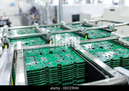 Green printed circuit boards in metal racks on a conveyor inside electronics factory showing automated high volume assembly and process control Stock Photo