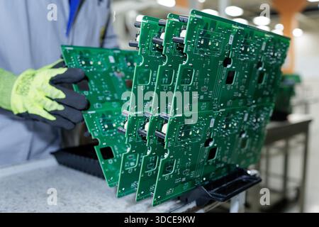 Factory worker in protective gloves handling large green printed circuit board panels during electronics assembly process Stock Photo