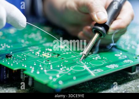 Close up of worker hand soldering components on green printed circuit board at electronics factory for repair and assembly concept Stock Photo