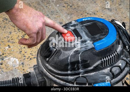 A hand pressing the power button on a dusty industrial vacuum cleaner. Stock Photo