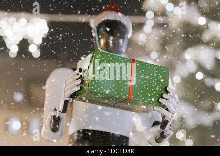 AI robot wearing a Santa hat, holding a Christmas present wrapped in green and red. Futuristic holiday concept in a snowy, festive setting with bokeh Stock Photo