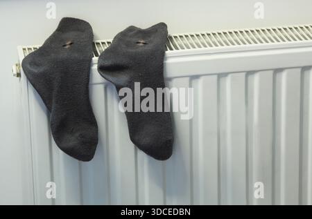 An everyday domestic scene with dark socks hanging on a modern radiator. The concept of home comfort, energy saving, drying laundry. Stock Photo