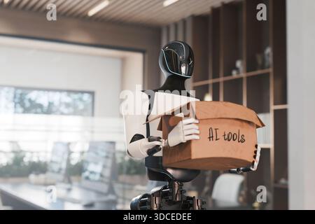 Humanoid robot holds a cardboard box labeled "AI tools" in a modern office. Concept of artificial intelligence implementation, technology, automation, Stock Photo