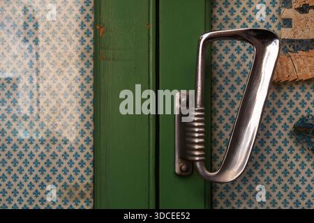 Vintage metal door handle on green wooden door with patterned wallpaper Stock Photo