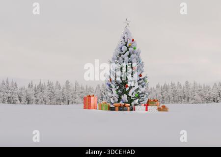 snow-covered Christmas tree, decorated with ornaments and surrounded by gifts, stands in a serene, vast winter landscape under a soft, overcast sky. H Stock Photo