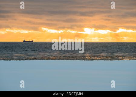 View of a distant ship silhouetted against a fiery sunset over the icy Baltic Sea, where the horizon blurs the line between water and sky, Parnu, Esto Stock Photo