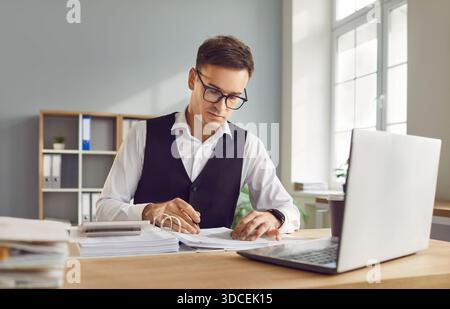 Focused serious man, young accountant calculator looking at laptop screen to calculate expenses Stock Photo