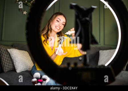 Influencer recording a beauty routine at home. She is using ring light and smartphone. Stock Photo