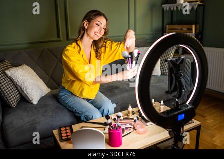 Influencer recording a beauty routine at home. She is using ring light and smartphone. Stock Photo
