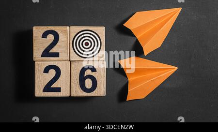2026 Happy New Year. Wooden cube block 2026 greeting card on Blackboard with 2 orange paper planes. Stock Photo