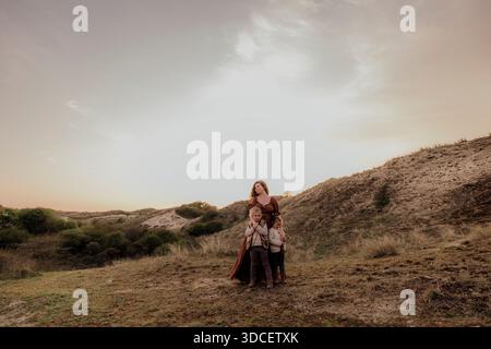 Woman and daughters in flowing dress cuddling on sandy path at dusk Stock Photo