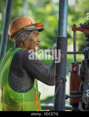 Indonesian worker in uniform and helmet at a machine in Bali Stock Photo