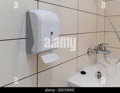 Close-up of a wall-mounted toilet paper holder box against a wall finished with large light ceramic tiles in a modern bathroom interior Stock Photo