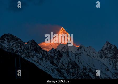 View of the radiant, snow-capped mountain peak glows with warm, orange light against the cool, deep blue sky, a majestic spectacle, Passu, Gilgit Balt Stock Photo