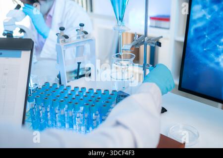 Two female scientists in white lab coats working together in a bright laboratory with microscopes, glassware, and blue test tubes, representing teamwo Stock Photo