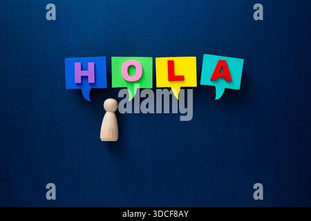 Wooden pawn and colorful speech bubbles spelling hola on a blue background representing communication Stock Photo