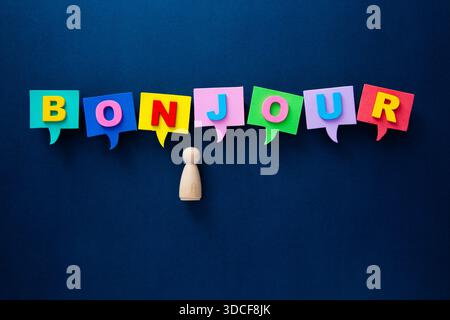 Wooden person figurine engaging with colorful speech bubbles showing bonjour on a dark blue background Stock Photo