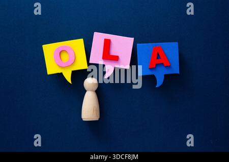 Wooden figurine communicating with hola word on speech bubbles against a blue background Stock Photo
