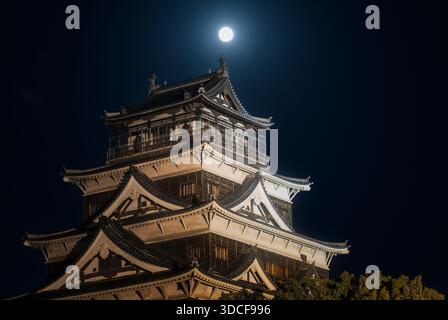 Hiroshima, Japan - 19 December 2025: View of the majestic Hiroshima Castle illuminated against the inky night sky, a full moon casting an ethereal glo Stock Photo