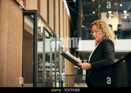 Mature businesswoman reading document while standing in law firm corridor Stock Photo