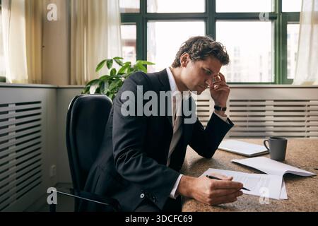 Concentrated male business expert examining agreement papers while sitting at table in law firm Stock Photo