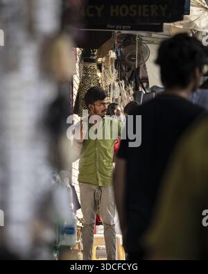 Mumbai, India - 06 June 2023: View of a man in a green shirt standing near Fancy Hosiery, amidst the bustling street life and muted tones of the city. Stock Photo