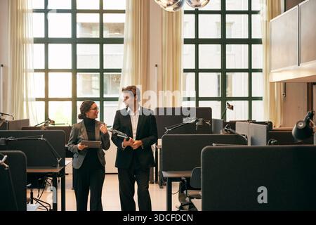 Male and female business professionals talking with each other while walking between office desks Stock Photo