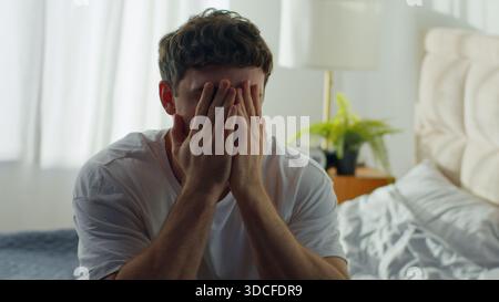 Despairing Caucasian man sitting on bed at home holding head in bedroom European male guy hopeless difficulties crisis grief anxiety distraught Stock Photo