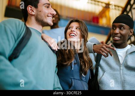 Low angle view of happy female student spending leisure time with male friends in college campus Stock Photo