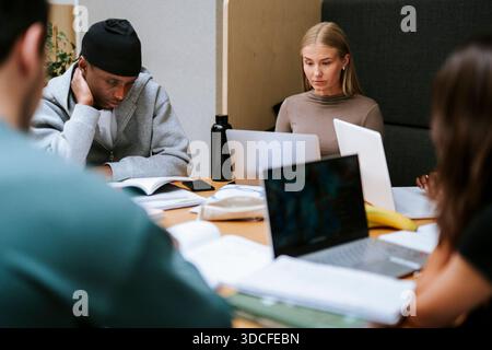 Focused male and female student studying while sitting at table in college campus Stock Photo