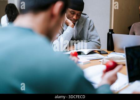 Focused male adult student leaning on elbow while studying in college campus Stock Photo