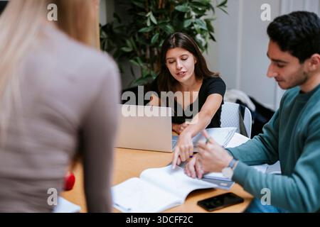 Young female student pointing on book while studying with male student in college campus Stock Photo