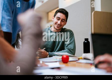 Smiling young male student studying with friends in university campus Stock Photo