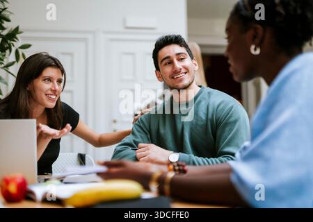 Smiling young man sitting with female friends in university campus Stock Photo
