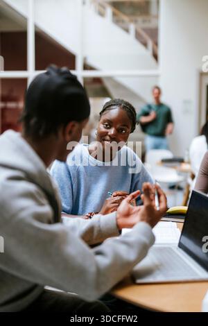 Smiling young woman listening to male friend sharing ideas while doing project in university campus Stock Photo