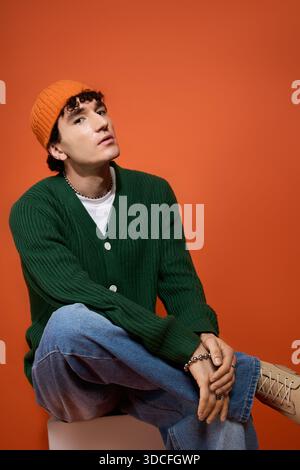 A handsome man in stylish attire sits confidently against a bright orange wall. Stock Photo
